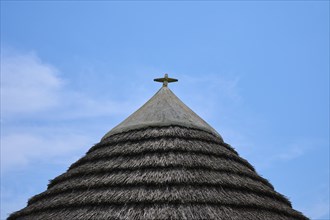 Traditional thatched roof in front of a clear blue sky with light clouds, summer,