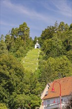 Small chapel on a hill in the forest, houses at the foot of the hill. Summer atmosphere,