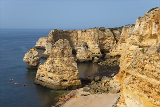 Majestic cliffs meet the calm sea on a sunny day with a golden sandy beach and blue sky, Praia da