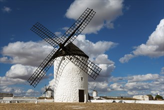 Historic white windmill under a blue sky with clouds and sunny surroundings in a wide landscape,