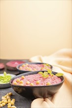 Hummus with beet and microgreen basil sprouts in ceramic bowl on a black concrete background and