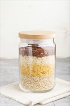 Glass jar with different kinds of rice poured in layers on a gray and white background. side view,