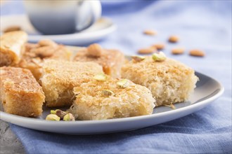 Traditional arabic sweets (basbus, kunafa, baklava) and a cup of coffee on a gray concrete