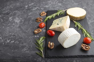 White goat cheese and various types of cheese with rosemary and tomatoes on black slate board on a