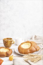 Sour cream bun with cup of coffee on a white wooden and concrete background and linen textile. Side