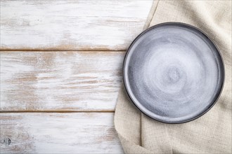 Empty gray ceramic plate on white wooden background and linen textile. Top view, copy space, flat