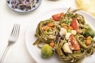 Tagliatelle green spinach pasta with tomato, pea and microgreen sprouts on a white wooden