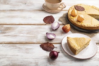 Autumn onion pie decorated with leaves and cup of coffee on white wooden background and linen