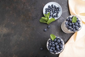 Yogurt with blueberry and chia in glass on black concrete background and orange linen textile. top