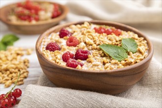 Wheat flakes porridge with milk, raspberry and currant in wooden bowl on white wooden background