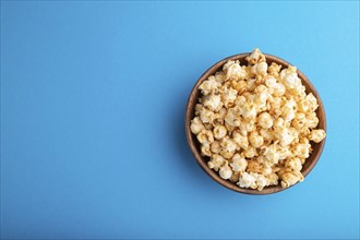 Popcorn with caramel in wooden bowl on a pastel blue background. Top view, flat lay, copy space