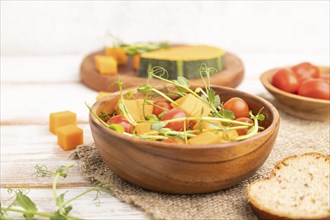 Vegetarian vegetable salad of tomatoes, pumpkin, microgreen pea sprouts on white wooden background