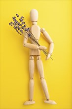 Wooden mannequin holding lavender flowers on yellow pastel background. close up, isolated, summer,