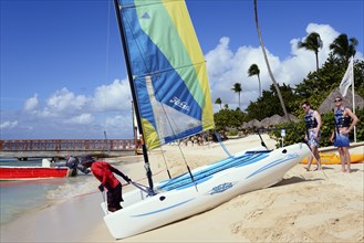 People rigging a catamaran on the beach under blue sky and palm trees, catamaran trip, Dominicus