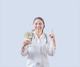 Smiling female doctor holding money and pointing up isolated. Happy young female doctor showing