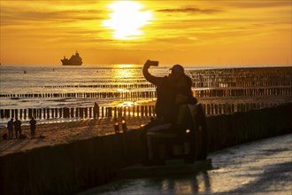 Sunset on the beach of Zoutelande, beach with wooden pile breakwaters, tourists, cargo ship sailing