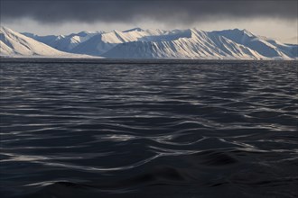 Snow-covered mountains, undulating sea surface, Woodfjord, Svalbard and Jan Mayen archipelago,