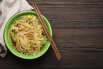 Asian noodles soup in green rustic ceramic bowl with wooden chopsticks top view on dark wooden