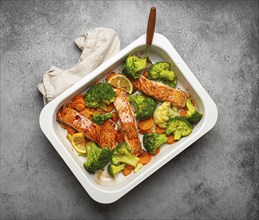 Top view of healthy baked fish salmon steaks, broccoli, cauliflower, carrot in casserole dish.