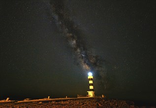 Lighthouse at night with radiant light, under a sky full of stars and the Milky Way, Colonia St.