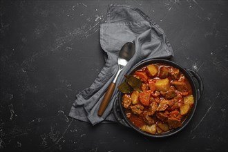 Beef meat stew with potatoes, carrot and delicious gravy in black casserole pot with bay leaves