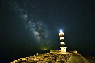 A nocturnal lighthouse next to the sea, under the starry sky and Milky Way, Colonia St. Jordi,