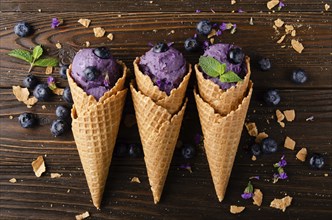 Flat lay view at wafer cones with blackberry icecream on wooden kitchen table