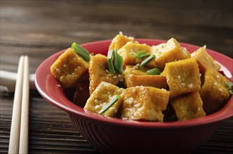 Crispy deep stir fried tofu cubes with chives in clay dish on wooden kitchen table