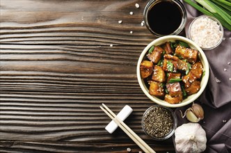 Flat lay view at stir fried tofu cubes with chives in clay dish on wooden kitchen table with napkin