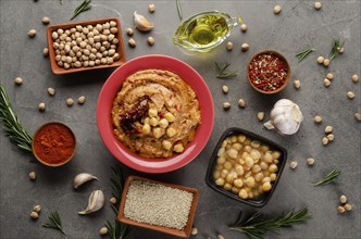 Hummus topped with chickpeas, olive oil and sun dried tomato on stone table with different spices