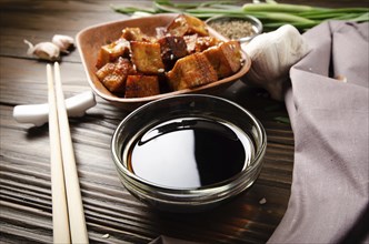 Crispy stir fried tofu cubes with chives in clay dish on wooden kitchen table with napkin chives