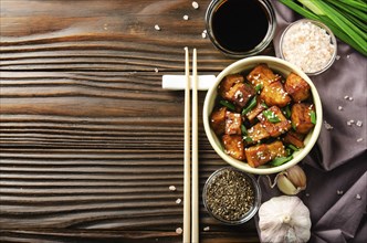 Flat lay view at stir fried tofu cubes with chives in clay dish on wooden kitchen table with napkin