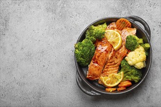 Healthy baked fish salmon steaks, broccoli, cauliflower, carrot in black cast iron casserole bowl