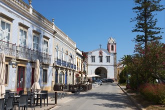 Cosy street lined with buildings and cafés, in the background a church under a clear sky, on the