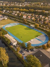 Sports field with blue running track, surrounded by residential area and autumnal trees, Nagold,