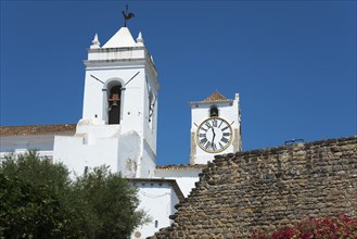 Two church towers with clocks, a wall in the foreground against a bright blue sky, Santa Maria do