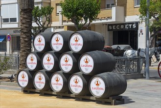 Several black barrels are stacked on a street in the city, Feria de la Manzanilla, Feria de