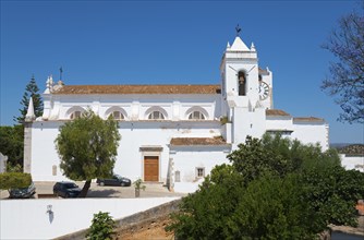 White painted church with bell tower surrounded by trees against a clear blue sky, Church of Santa