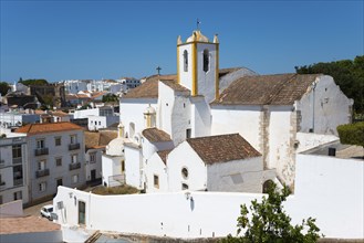 White church under a blue sky in a Mediterranean town with red roofs, Igreja de Santiago church,