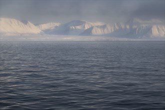 Snow-covered mountains, slightly undulating sea surface, Woodfjord, Svalbard and Jan Mayen