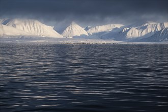 Snow-covered mountains, undulating sea surface, Woodfjord, Svalbard and Jan Mayen archipelago,