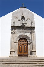 Historic church façade with detailed stonework and wooden door under a blue sky, Igreja da