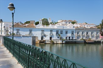 Bridge with green railing along a calm river, historical buildings in the background, Ponte Romana,