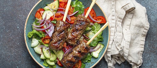 Grilled skewer meat beef kebabs on sticks served with fresh vegetables salad on plate on rustic