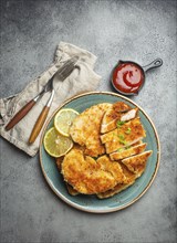 Crispy panko breaded fried chicken fillet with green salad and lemon cut on plate on gray rustic