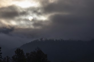 Sun above a mountain range breaking through morning clouds and fog, Leoben, Styria, Austria, Europe