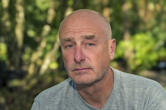 Portrait, man, camera view, sad, beard, unshaven, bald, background blurred, edge of forest,