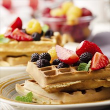 CLoseup view at belgian waffles served with strawberries and blackberries on kitchen table