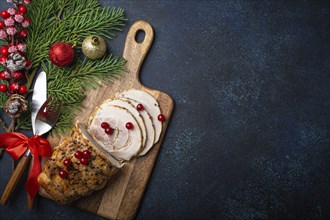 Christmas baked ham sliced with red berries and festive decorations on wooden cutting board, dark