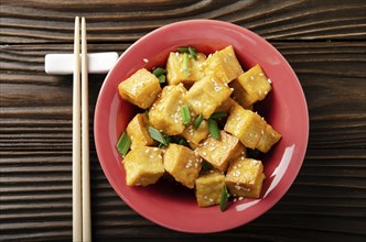 Flat lay view at crispy deep stir fried tofu cubes with chives in clay dish on wooden kitchen table